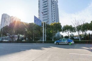 A street scene with a blue car, a tall building, and a clear sky.
