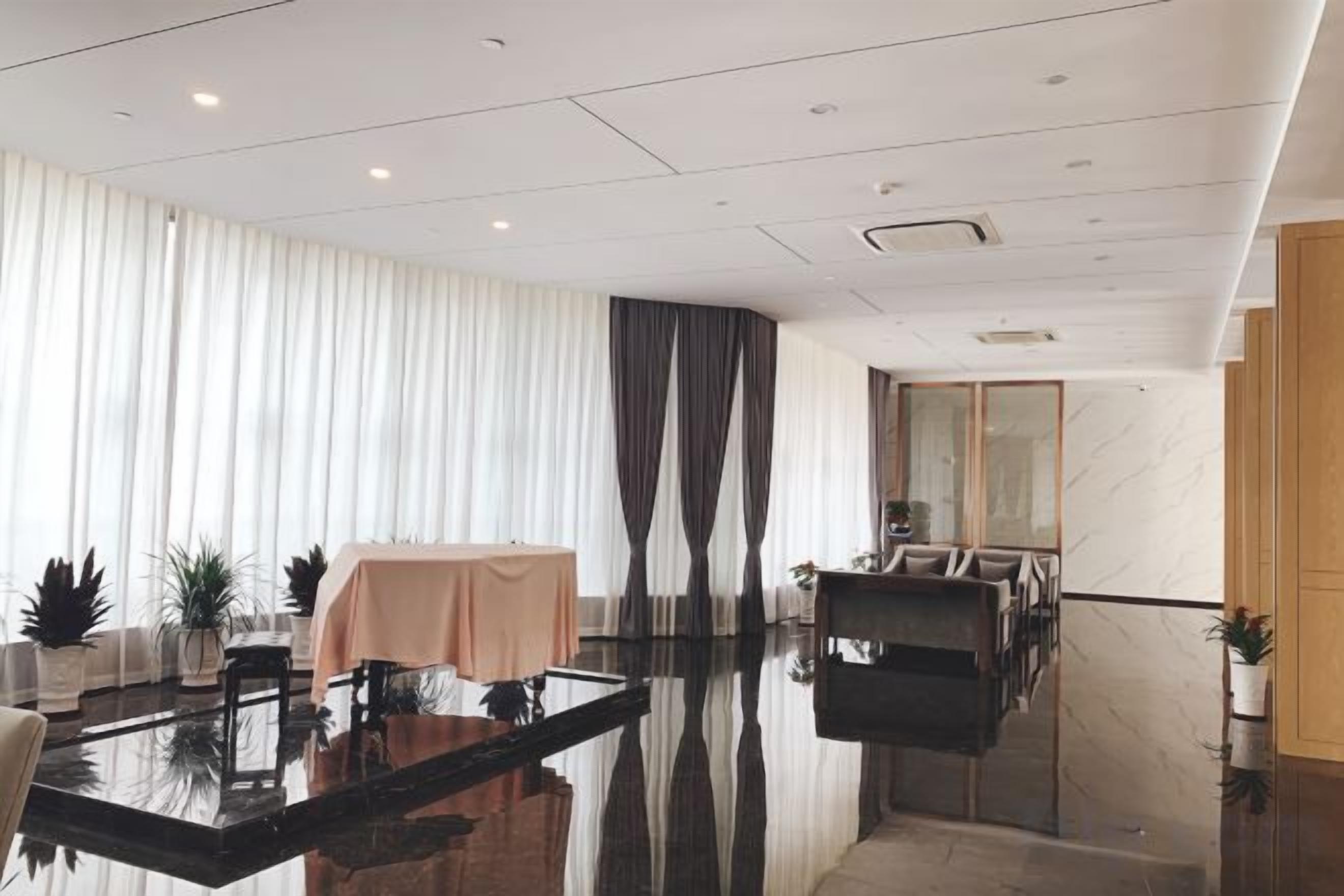 Een moderne hotellobby met een glazen tafel, een zithoek en een groot raam met gordijnen.