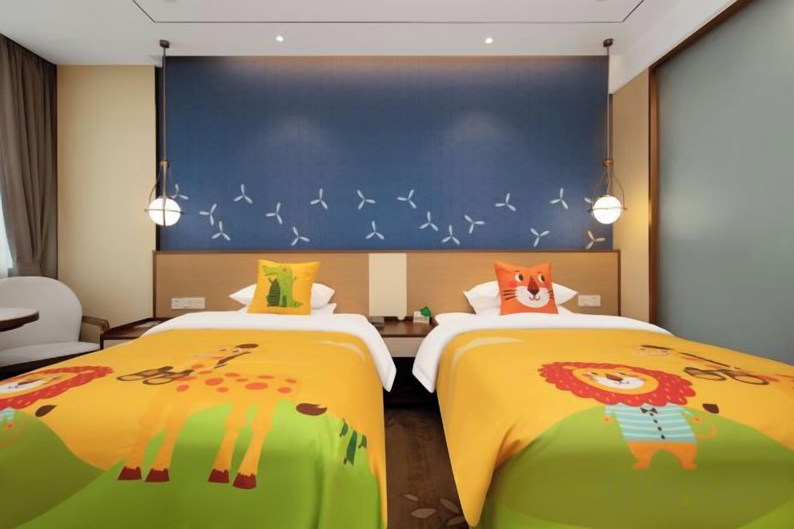 A hotel room with two beds, each with a colorful bedspread, a large wall mural, and a seating area with a chair and table.