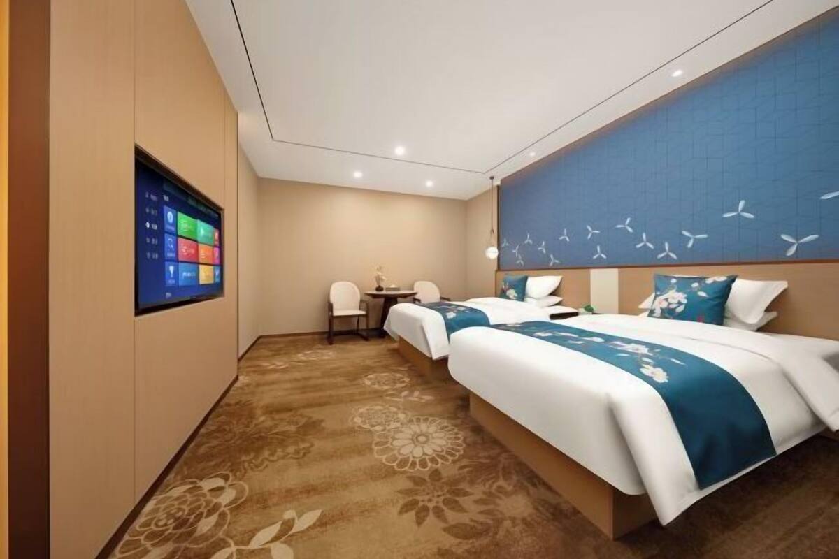 Una camera d'albergo con un grande schermo digitale, due letti, una scrivania e una sedia.