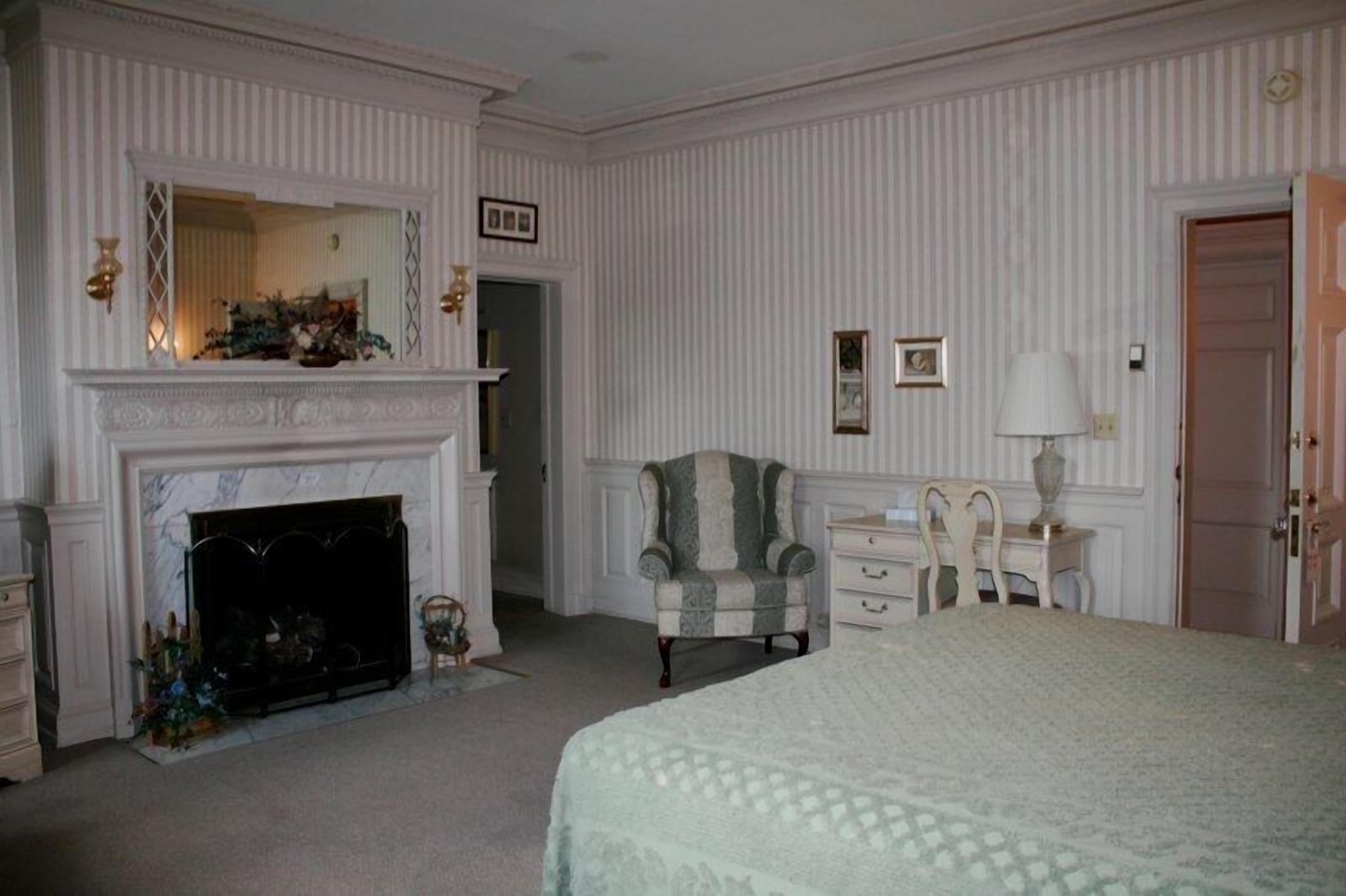 A bedroom with a fireplace, a bed, a chair, a nightstand, and a door.