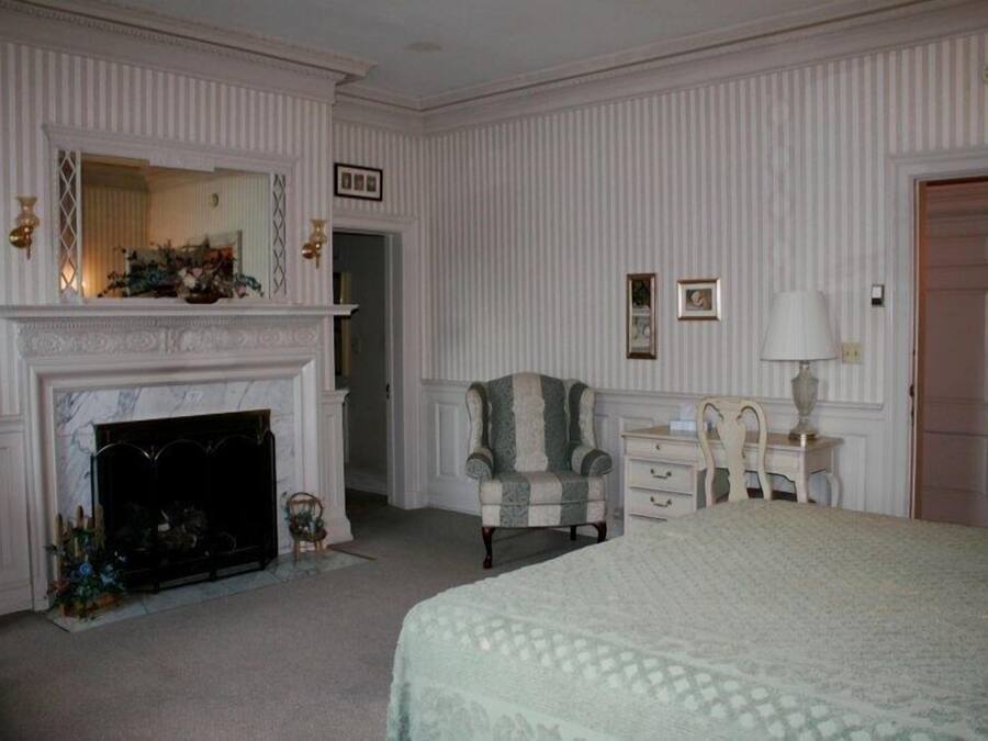 A bedroom with a fireplace, a bed, a chair, a nightstand, and a door.