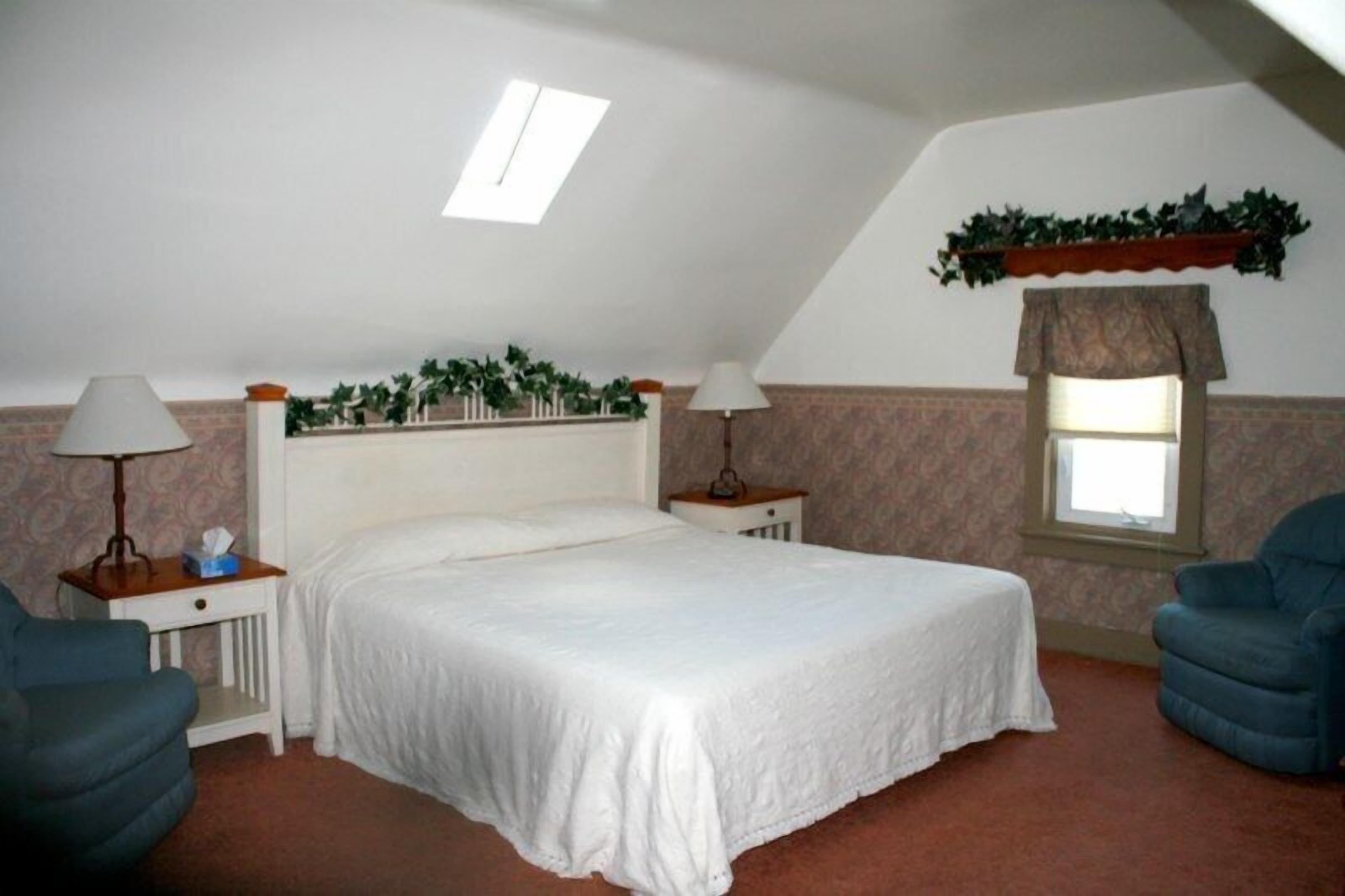 Un dormitorio con una cama individual, dos mesitas de noche, una lámpara de noche, una ventana con cortina y un ventilador de techo.