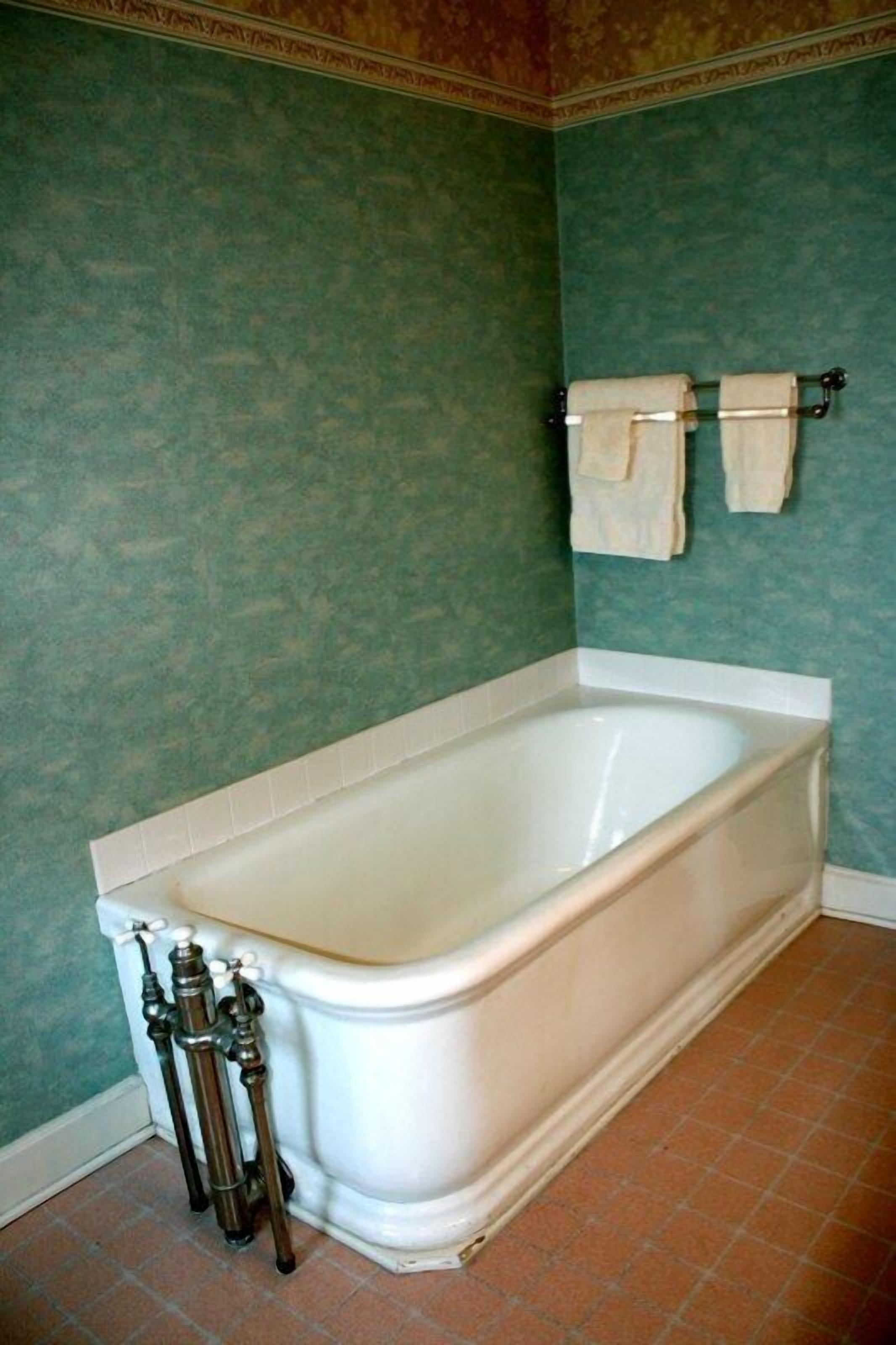 Un baño con una bañera blanca, paredes verdes y suelo de baldosas.