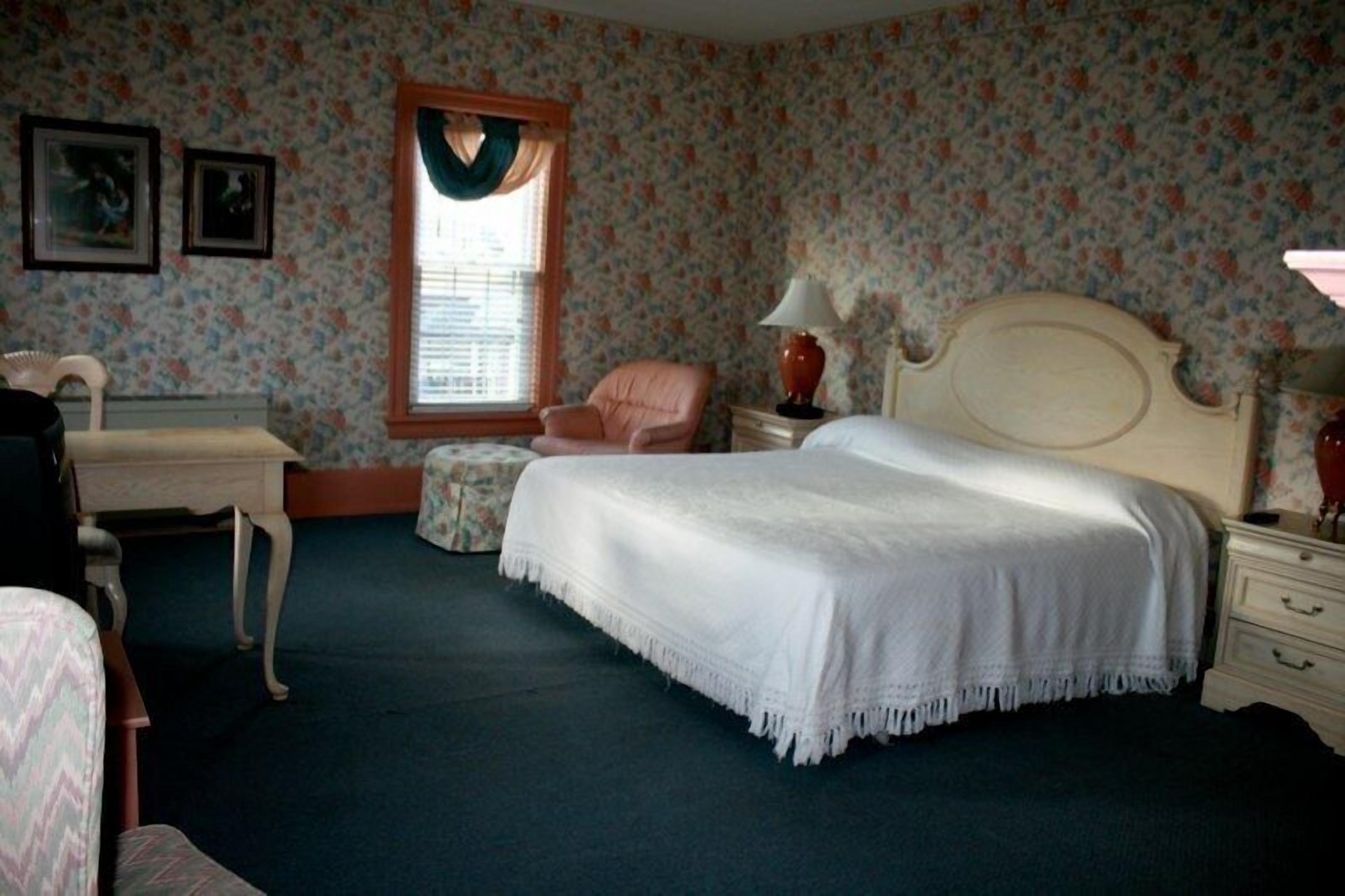A bedroom with a bed, a chair, a dresser, and a window with curtains.