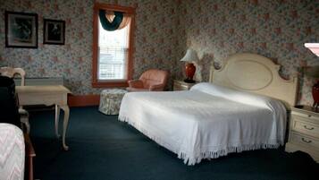 A bedroom with a bed, a chair, a dresser, and a window with curtains.