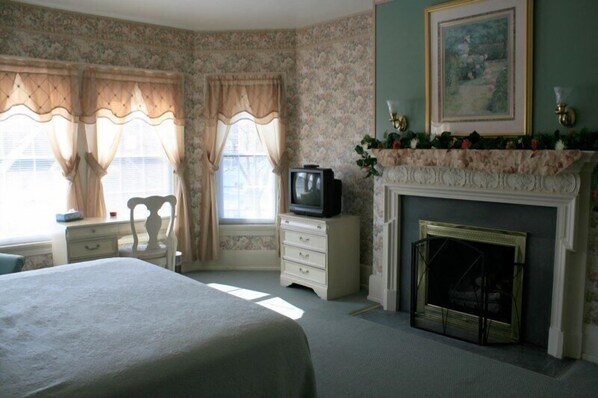 Un dormitorio con cama, cómoda, televisor, chimenea y papel tapiz floral.