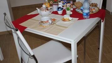 A dining table set with a teapot, cups, a water bottle, and a plate of food.