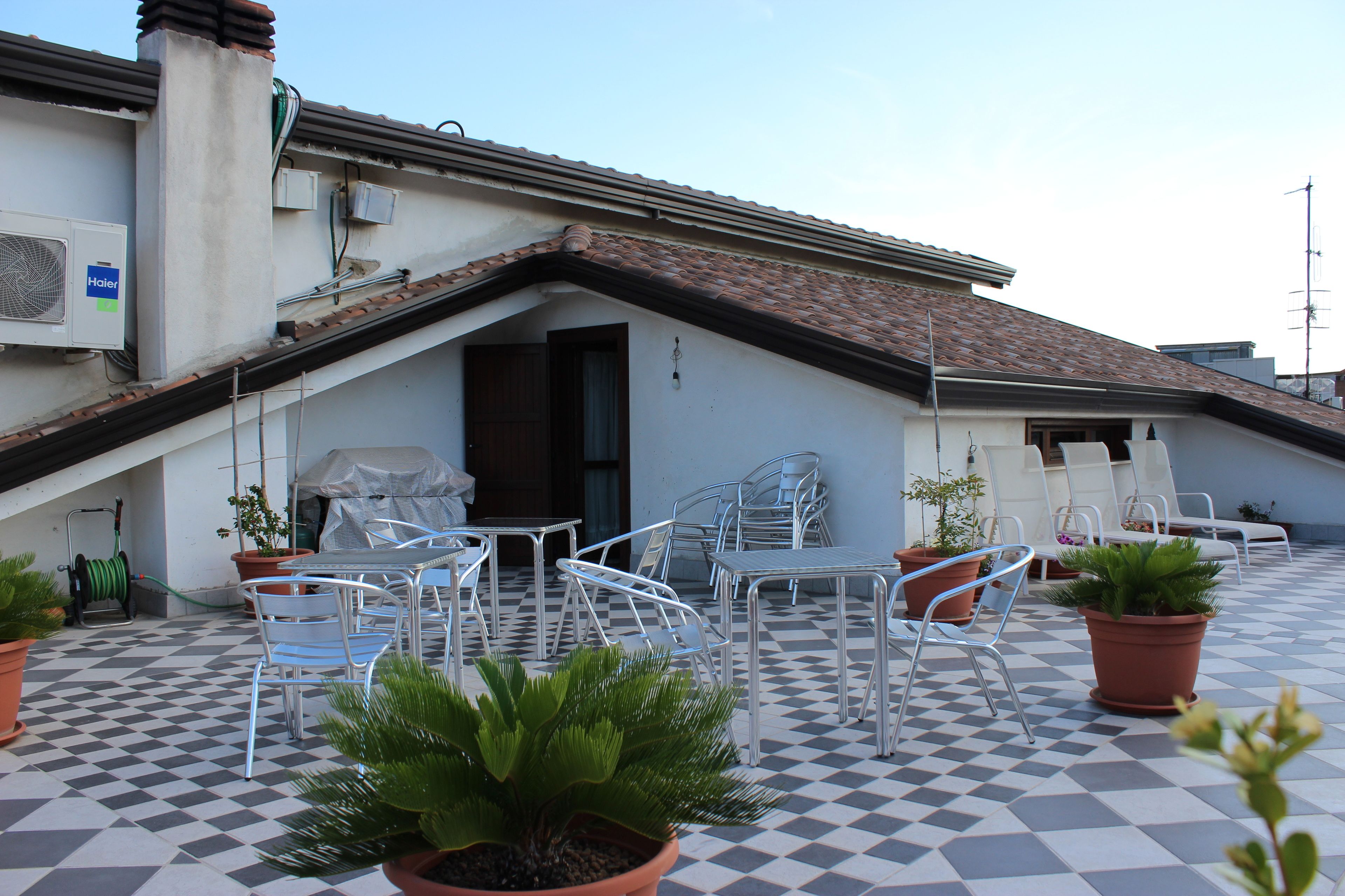 A rooftop patio with checkered flooring, metal chairs, and potted plants.