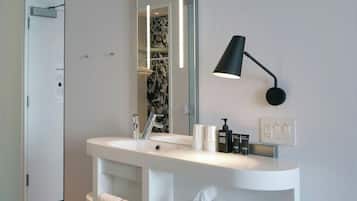 A modern bathroom with a white vanity, a large mirror, a black wall-mounted lamp, and a wooden floor.