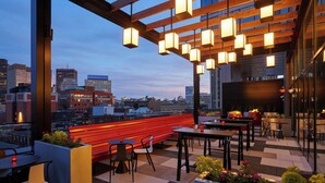 Una terraza en la azotea con un banco rojo, mesas, sillas y luces colgantes.