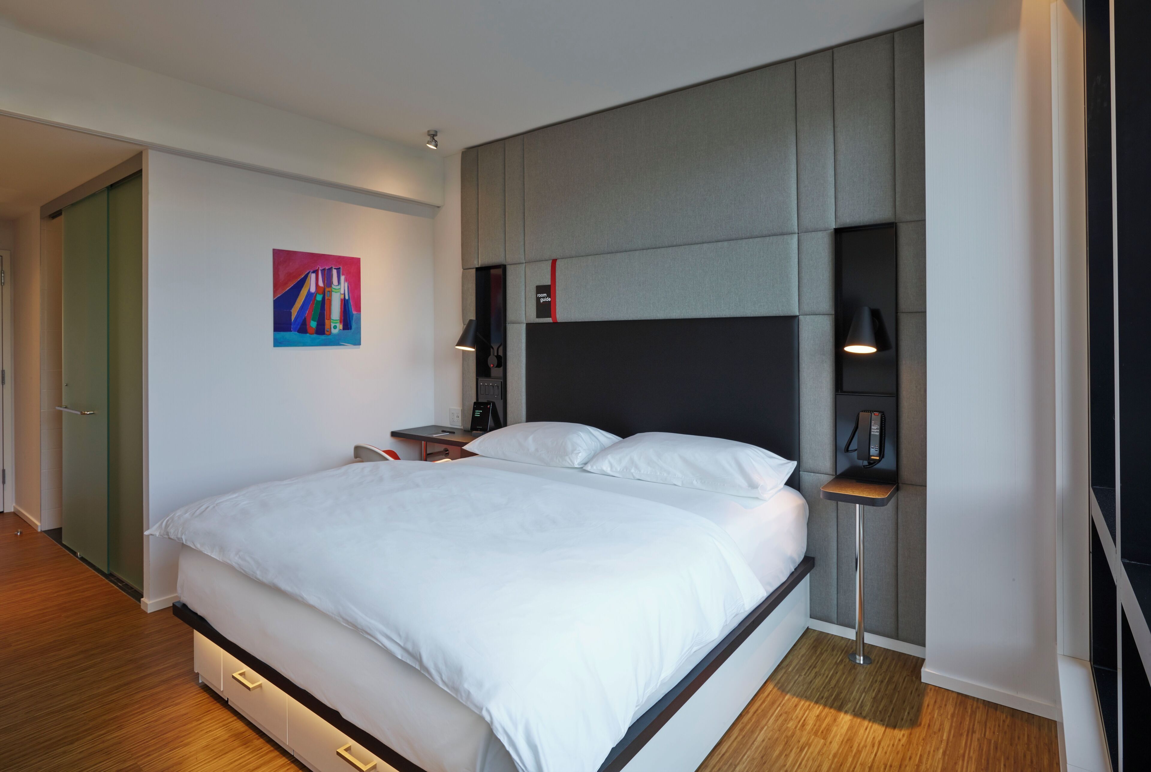 A modern bedroom with a large bed, bedside tables, a nightstand, and a painting on the wall.