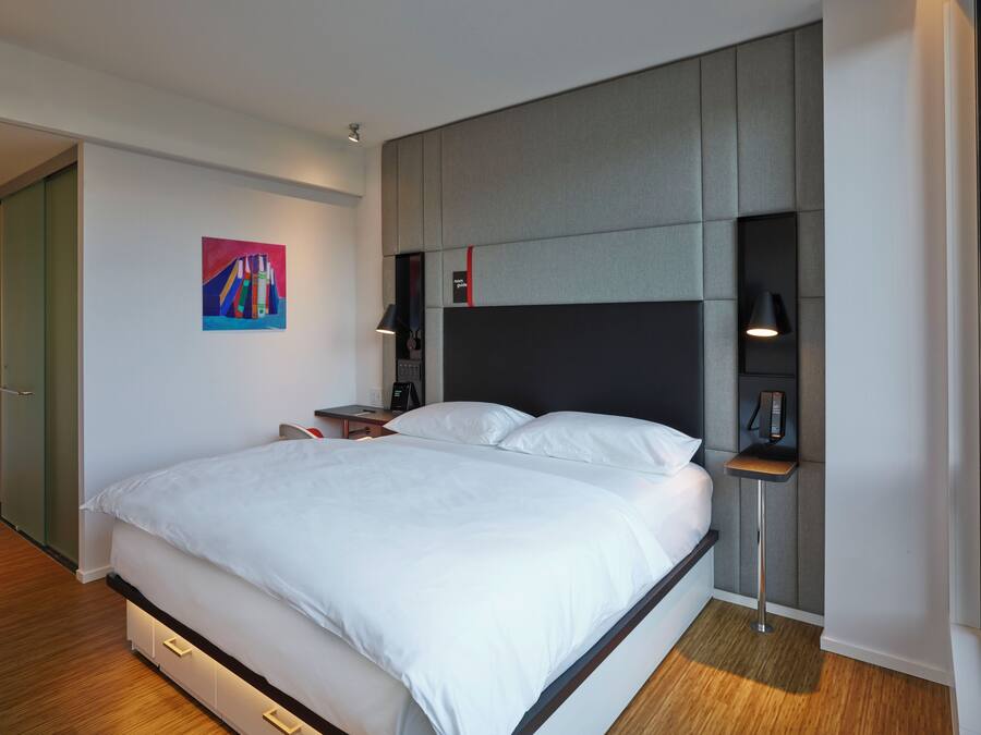 A modern bedroom with a large bed, bedside tables, a nightstand, and a painting on the wall.