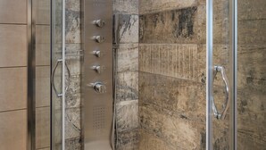 Une douche moderne dotée d’une porte en verre, d’un pommeau de douche à effet pluie et d’un panneau de commande.
