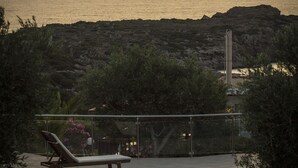 Une piscine dotée de chaises longues et d’un espace salon en contrebas, entourée de végétation et offrant une vue sur une côte rocheuse.