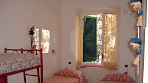 A bedroom with bunk beds, a window with green shutters, and a small table with a lamp.