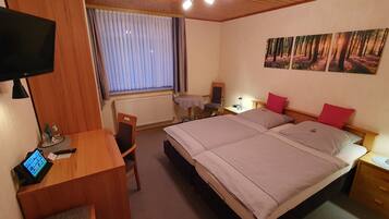 A hotel room with a bed, bedside table, lamp, desk with a computer, chair, and a TV.