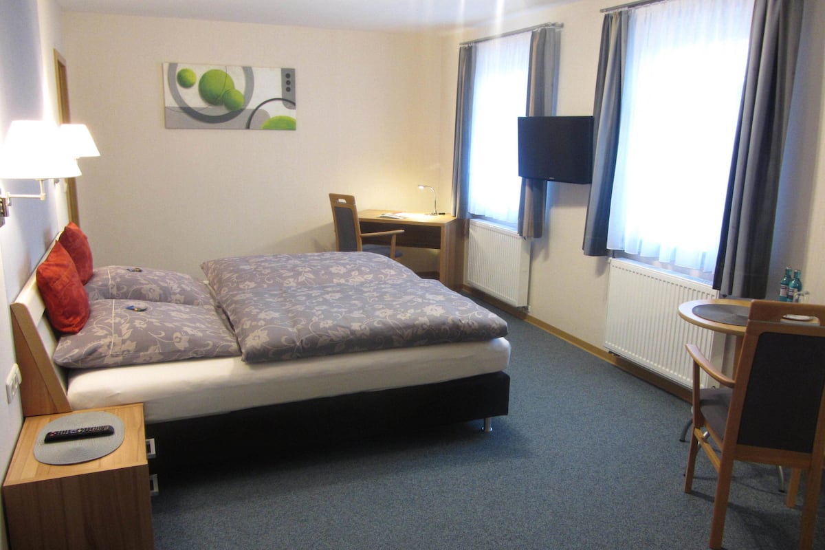 Une chambre d’hôtel avec un lit, un bureau, une chaise, une télévision et un tableau au mur.