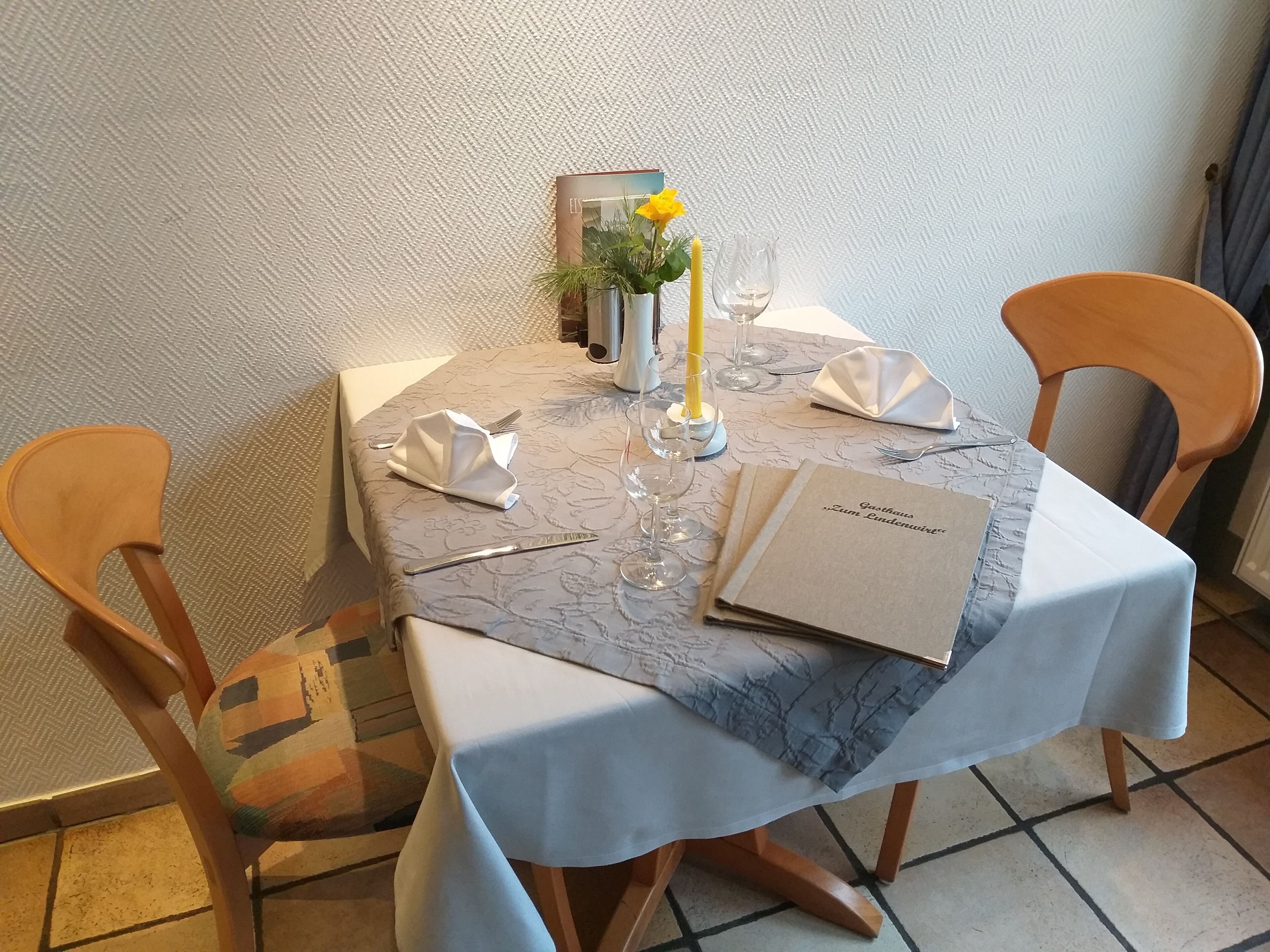 A dining table set with a white tablecloth, a menu, and a candle.