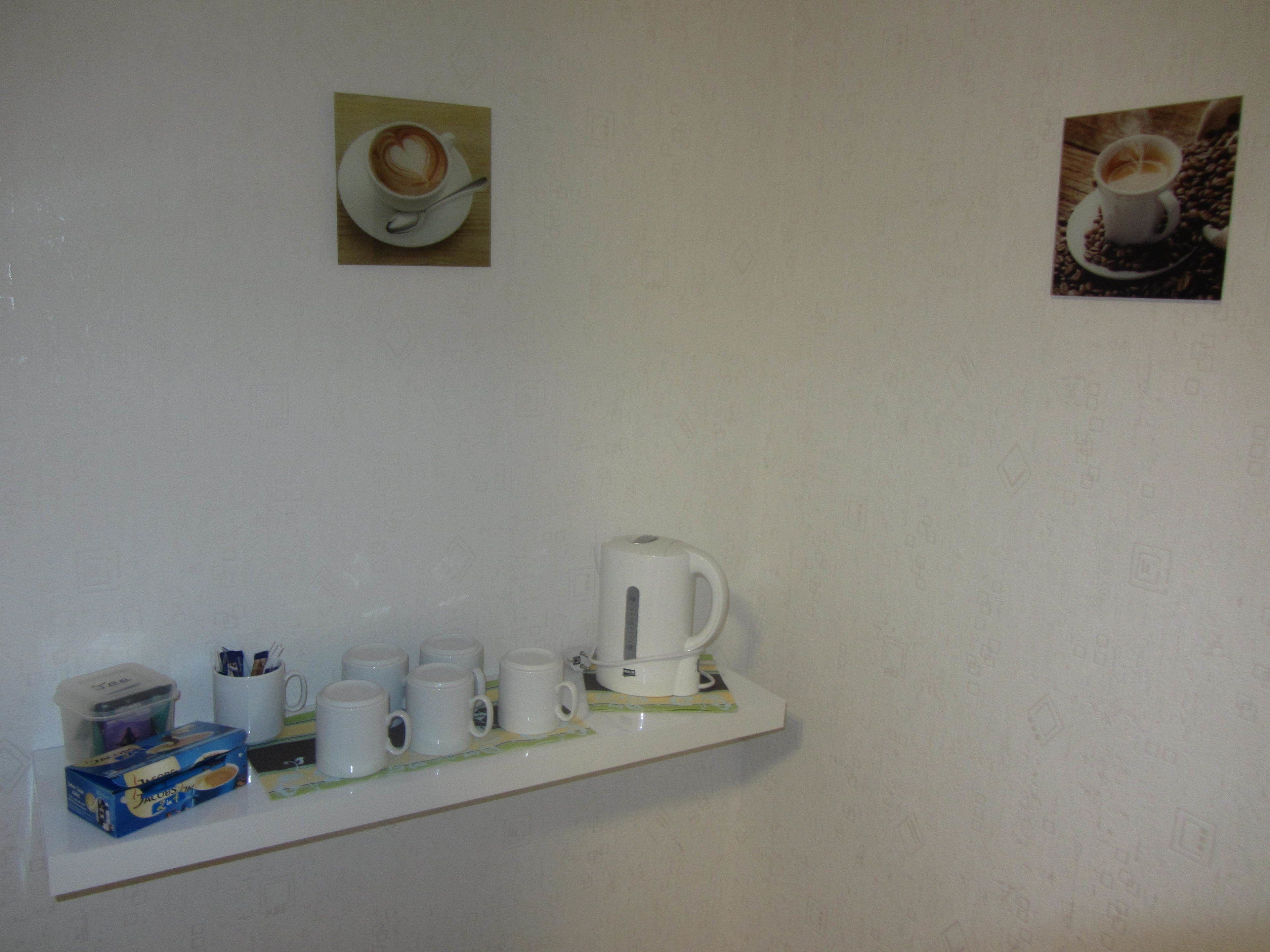 Ein weißes Regal mit einer Kaffeemaschine, mehreren weißen Tassen und einer Kapselbox.
