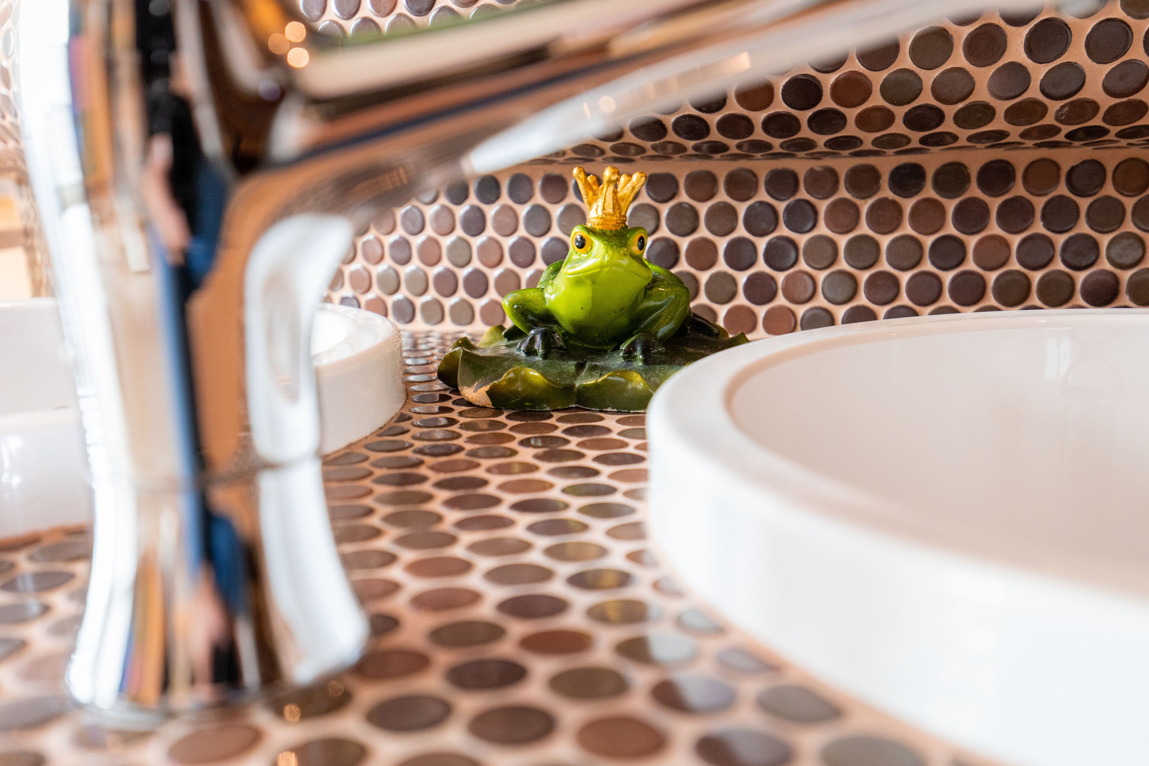 Un baño con lavamanos, grifo y una estatua decorativa de un sapo.