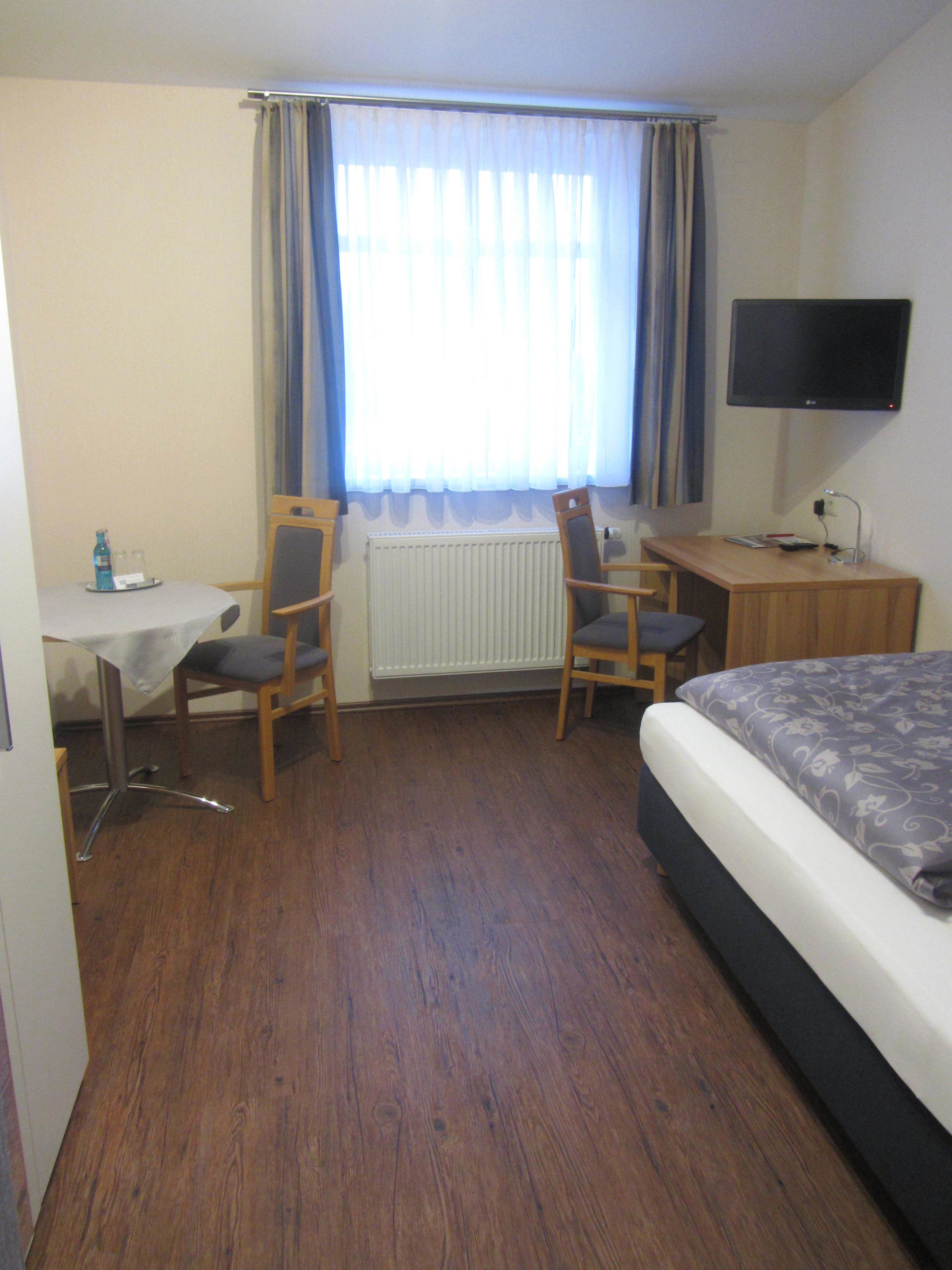 Une chambre d’hôtel avec un lit, un bureau et une chaise, une télévision et une fenêtre avec des rideaux.