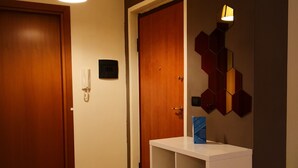A hallway with two wooden doors, a white console table with a blue book, and a wall-mounted hexagonal light fixture.