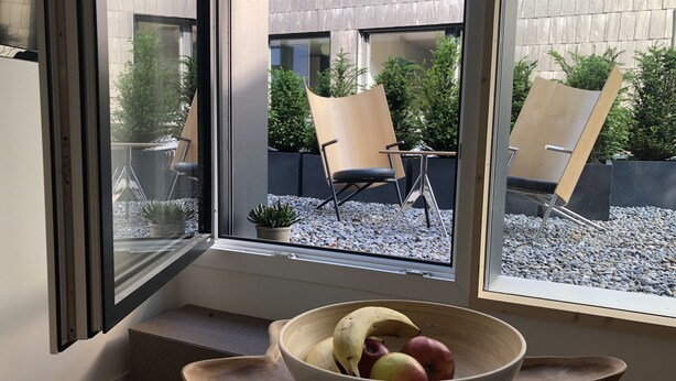 Una habitación moderna con un ventanal grande, una mesa de madera y un frutero con fruta.