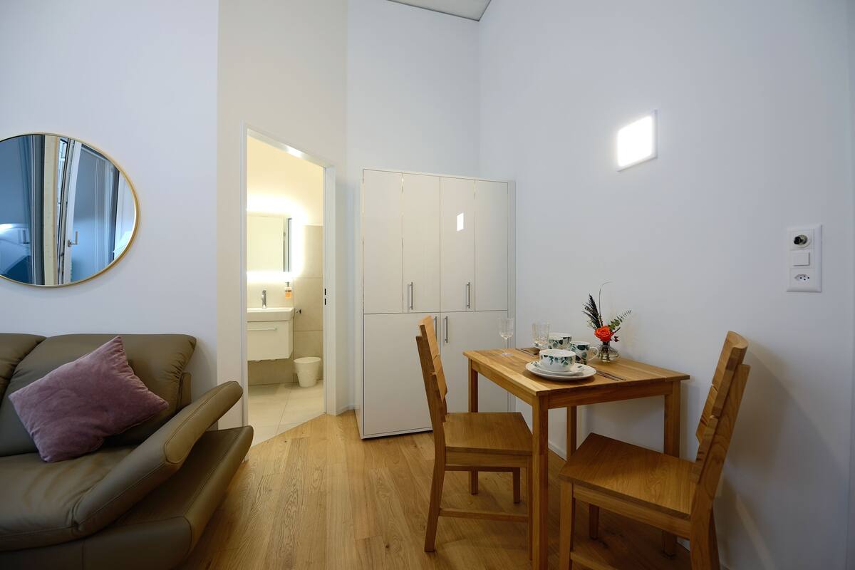 A compact living space with a sofa, a dining table with chairs, a mirror, and a wardrobe.