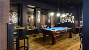 Una mesa de billar en una habitación con suelo de madera, una zona de bar con taburetes y cuadros en la pared.
