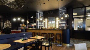 Un restaurante moderno con mesas y sillas de madera, una zona de bar y un área de estar con un sofá y una pequeña mesa.