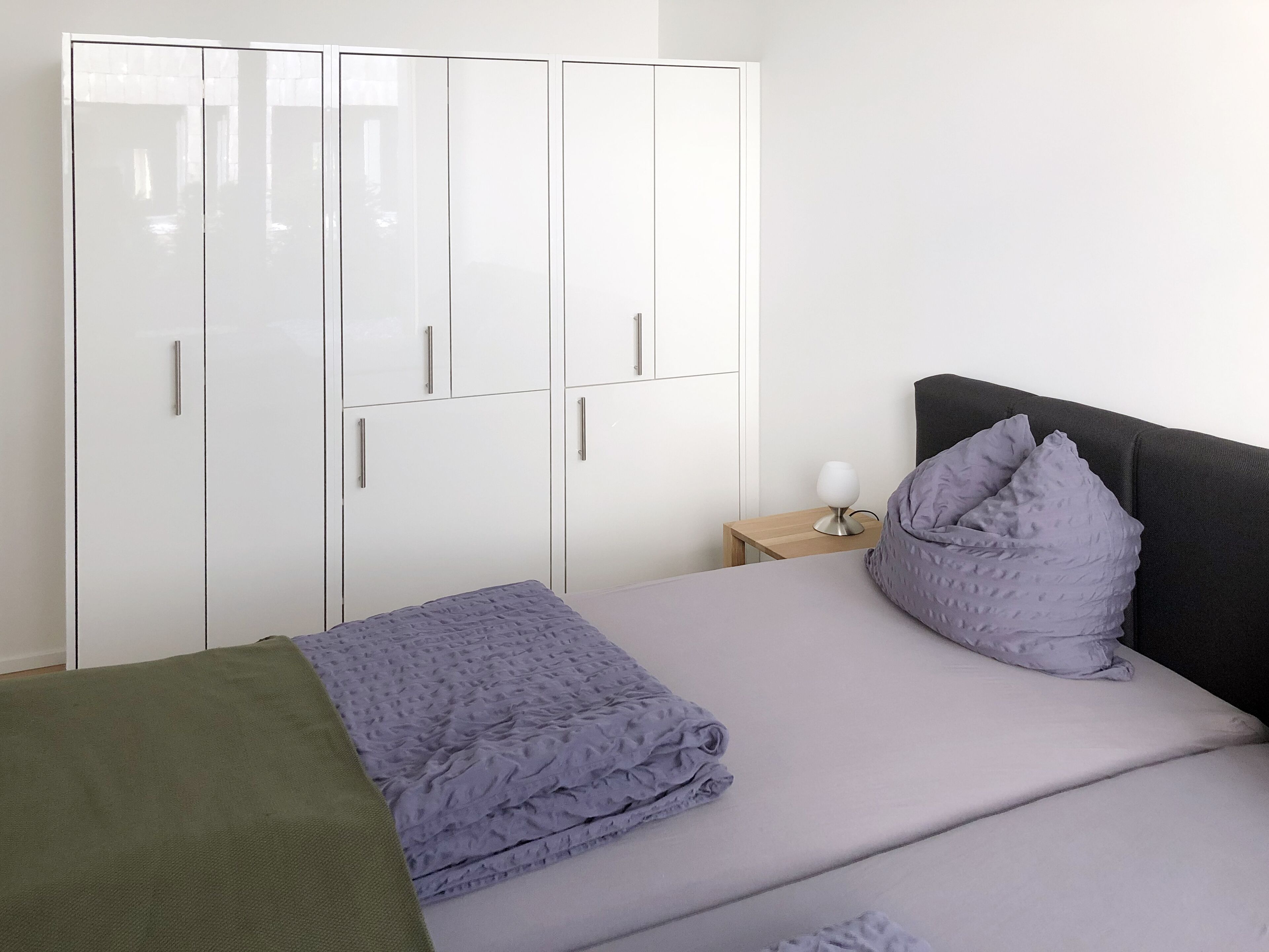 A bedroom with a bed, pillows, a bedside table, and a wardrobe.