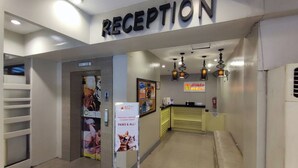 A reception area with a sign reading "RECEPTION" above the entrance. There are hanging lights, a counter with a sign for 'L'ecoter', and a poster advertising 'Bringing comfort to every guest' with a cat image. - Ecotel by L'Fisher (Bacolod)