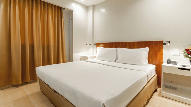 A hotel room with a large bed, a nightstand with a phone, and a wall-mounted light. - Ecotel by L'Fisher (Bacolod)