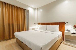 Una habitación de hotel con una cama grande, una mesita de noche con un teléfono y una lámpara fijada a la pared.