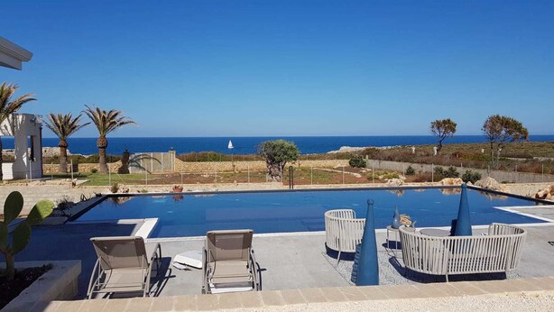 Una piscina con sillones de descanso y vistas al mar.