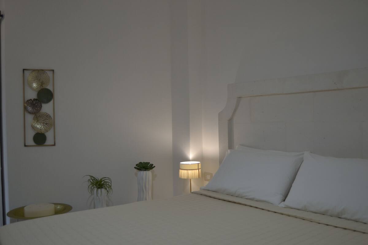 A bedroom with a bed, a bedside table, a lamp, and wall decorations.