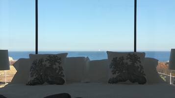 A bed with two decorative pillows and a view of the sea through large windows.
