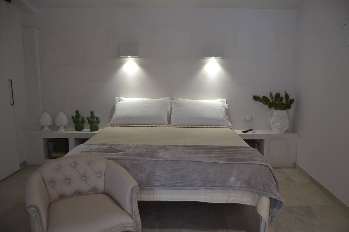 A bedroom with a bed, two bedside tables, a chair, and a potted plant.