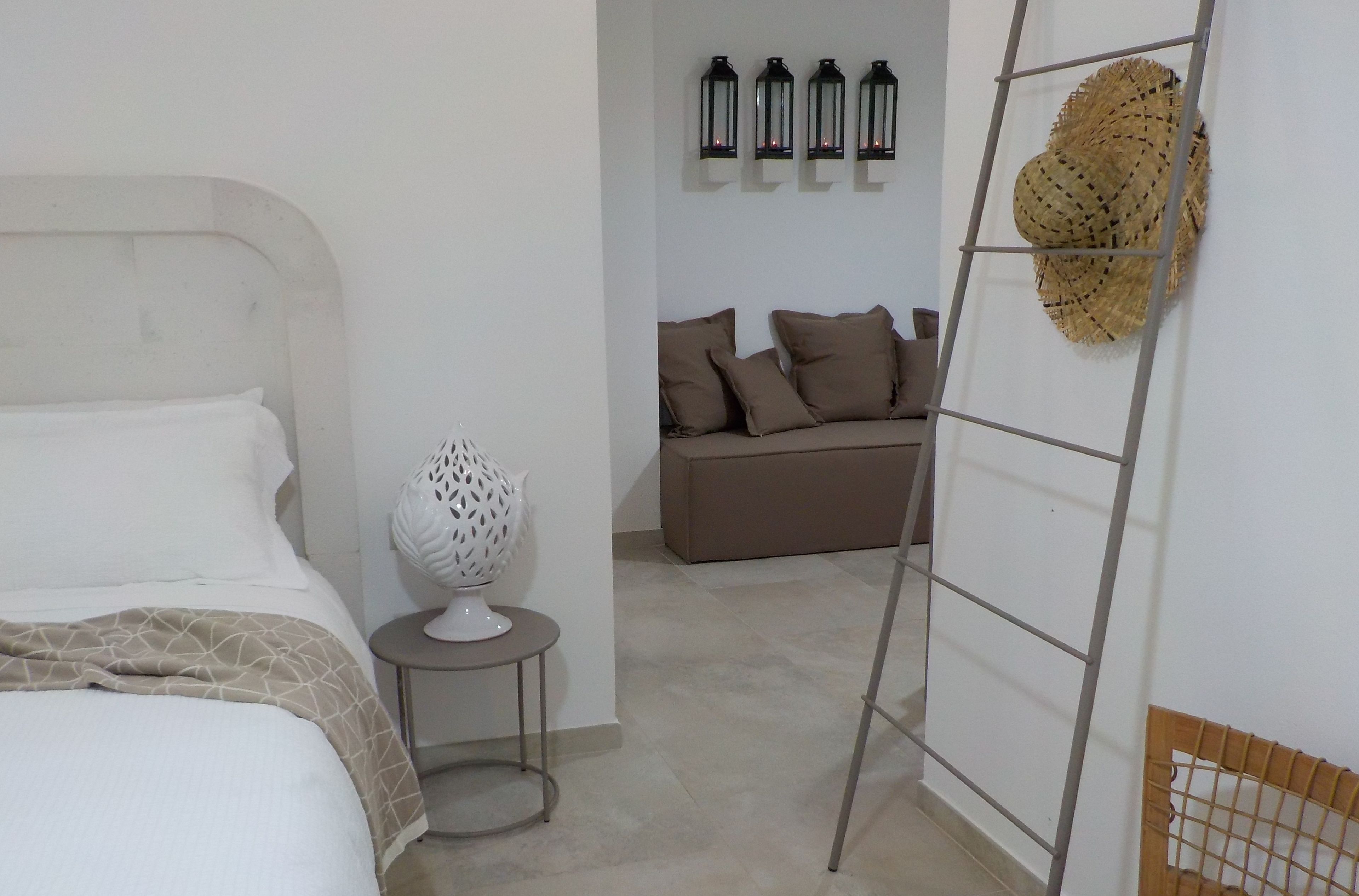 Un dormitorio con cama, una mesita con un objeto decorativo, un sofá con cojines y una escalera apoyada en la pared.