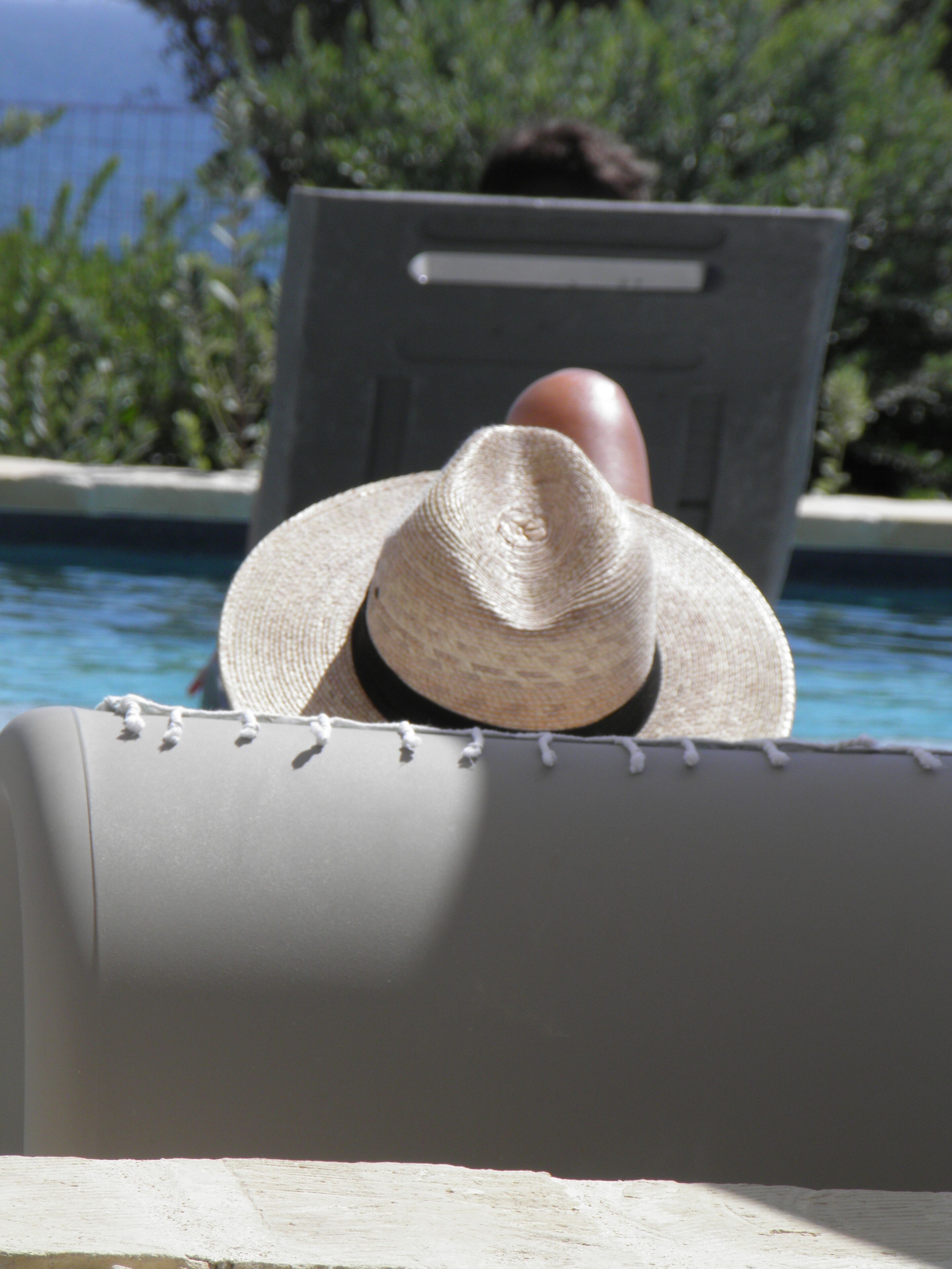 Un área junto a la piscina con una silla de descanso y una persona con sombrero de paja.