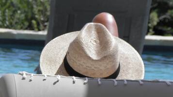 Un área junto a la piscina con una silla de descanso y una persona con sombrero de paja.