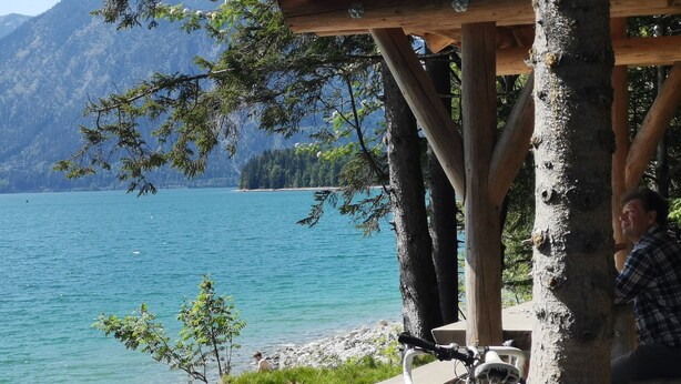 A wooden gazebo overlooking a lake with mountains in the background. - Ferienwohnung Landhaus alpinum (Lenggries)