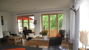 A modern living room with a sofa, a dining table, and a kitchen area with a stove. - Ferienwohnung Landhaus alpinum (Lenggries)