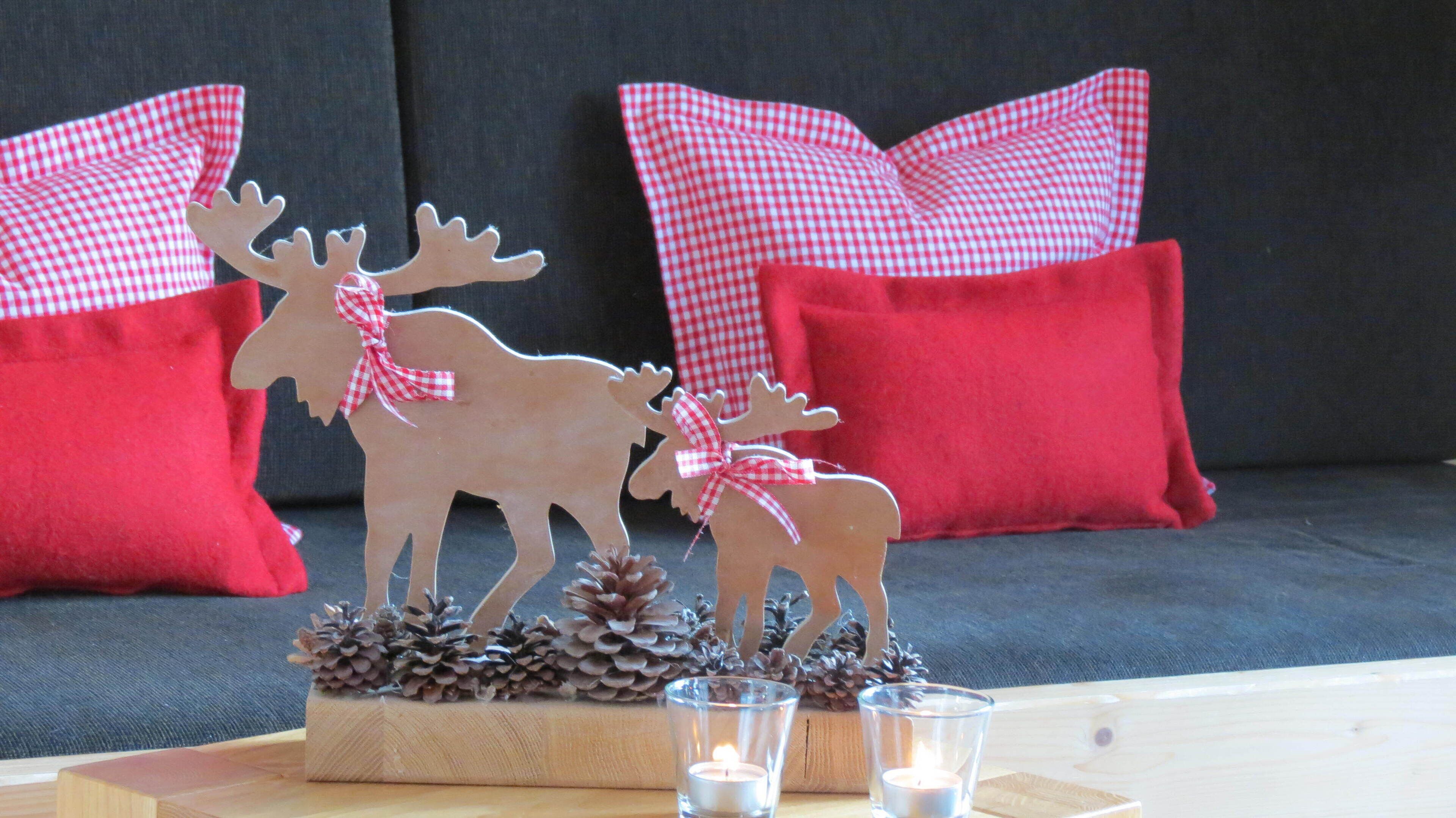 A decorative wooden reindeer with pinecones on a wooden base, placed on a table with candles.