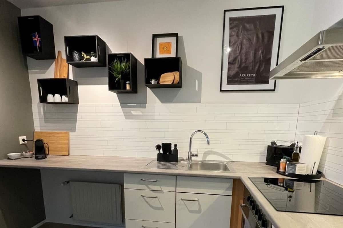 A modern kitchen with white subway tiles, black storage units, a stainless steel sink, and a black stove.