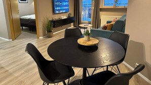 A modern living room with a round black table, black chairs, a TV on the wall, a balcony with a view, and a bed in the background. - Saga Apartments (Akureyri)