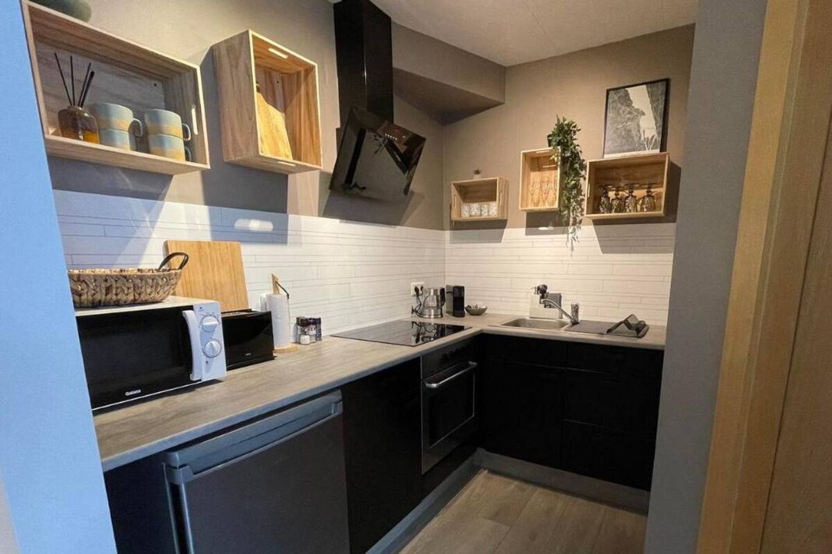 A compact kitchen with black cabinets, a microwave, a sink, and wooden shelves with various items.