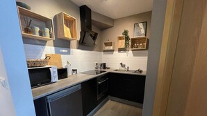 A compact kitchen with a microwave, toaster, sink, and wooden cabinets. - Saga Apartments (Akureyri)
