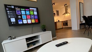 A modern living room with a flat-screen TV mounted on the wall, a white entertainment unit below, and a remote control on a white table. - Saga Apartments (Akureyri)